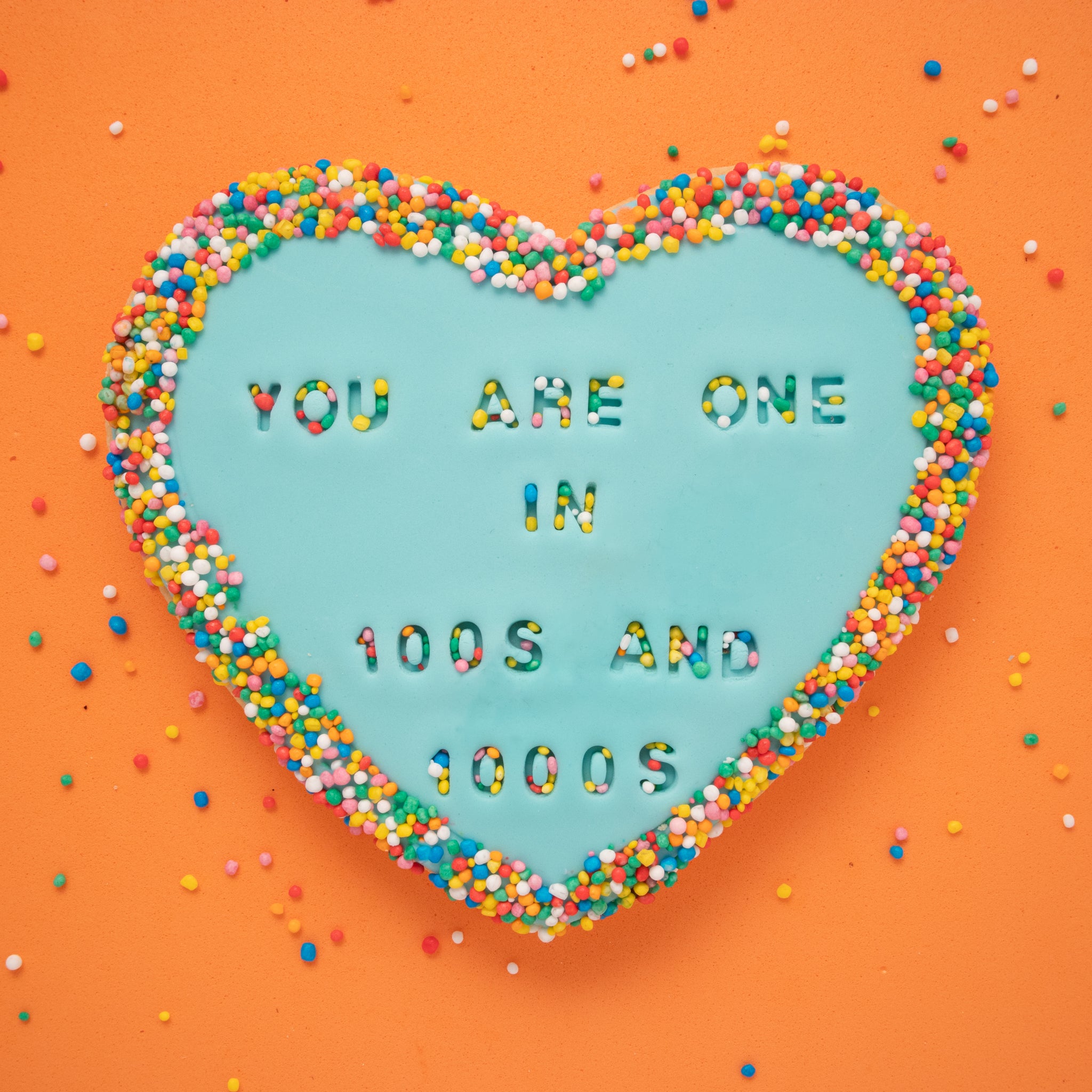 sugar cookie with blue fondant embossed with 'you are one in 100's and 1000's' on an orange background