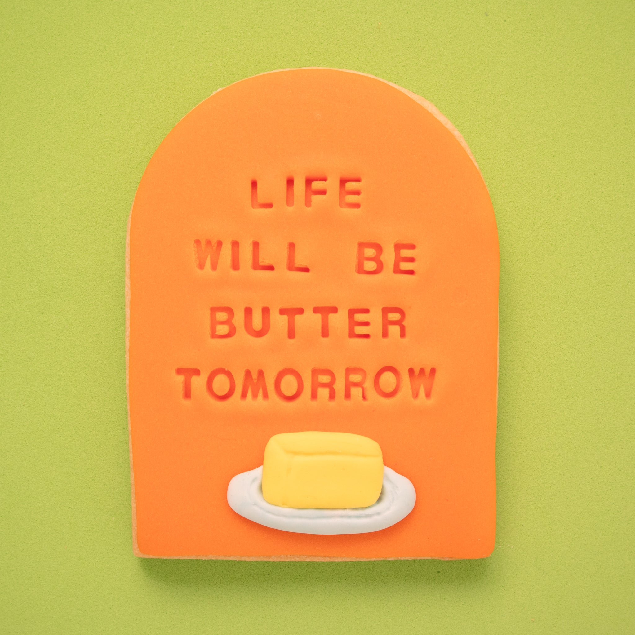 sugar cookie with orange fondant embossed with 'life will be butter tomorrow' on a green background