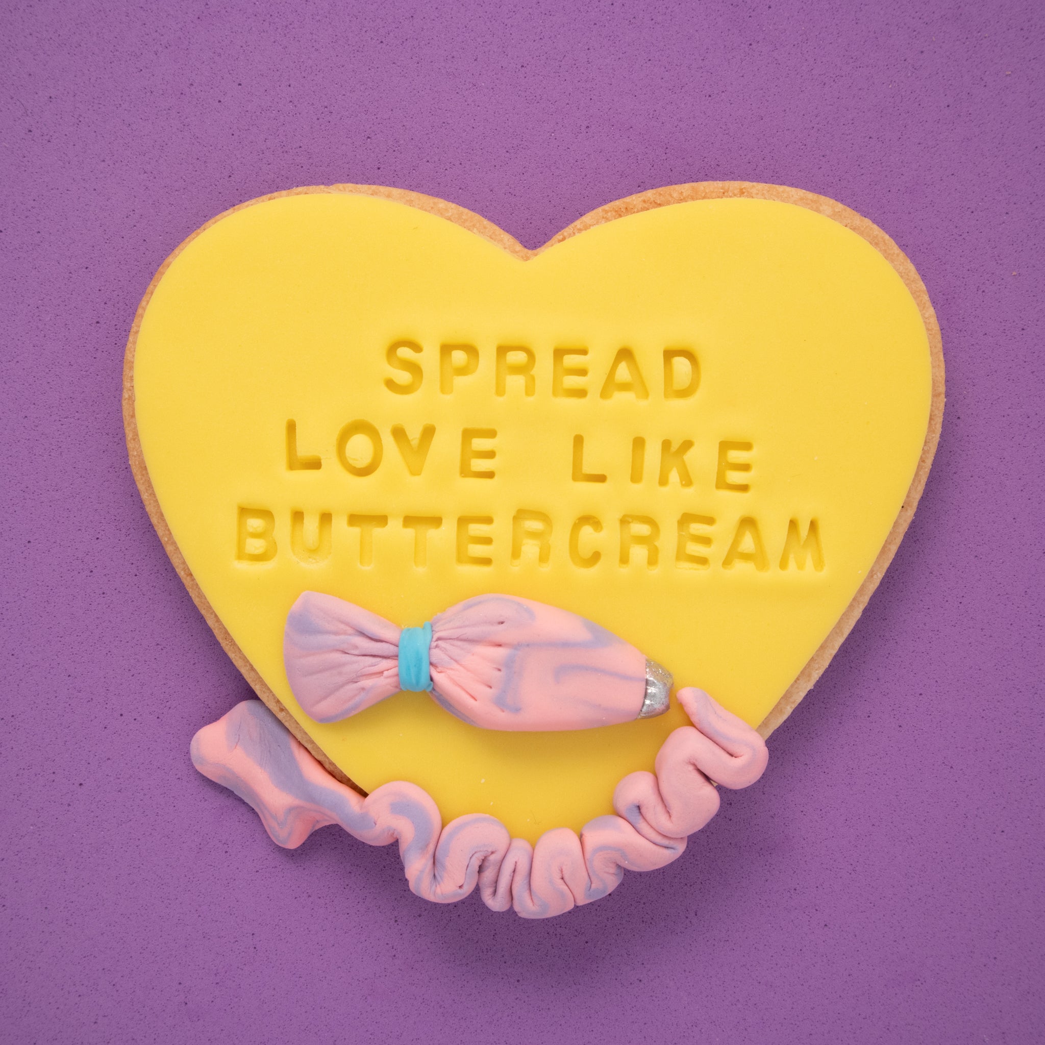 sugar cookie with yellow fondant embossed with 'spread love like buttercream' on a purple background