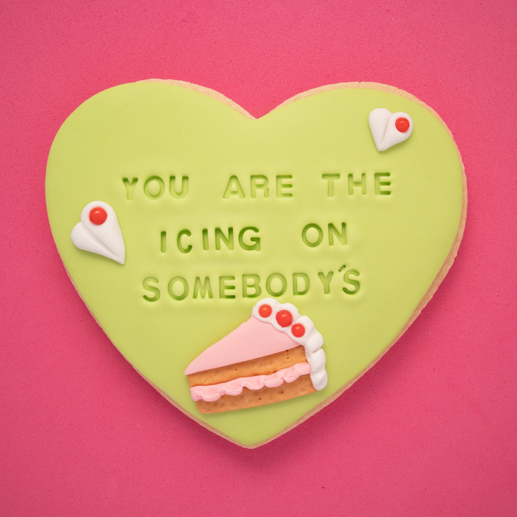 sugar cookie with green fondant embossed with 'you are the icing on somebody's cake' on a pink background